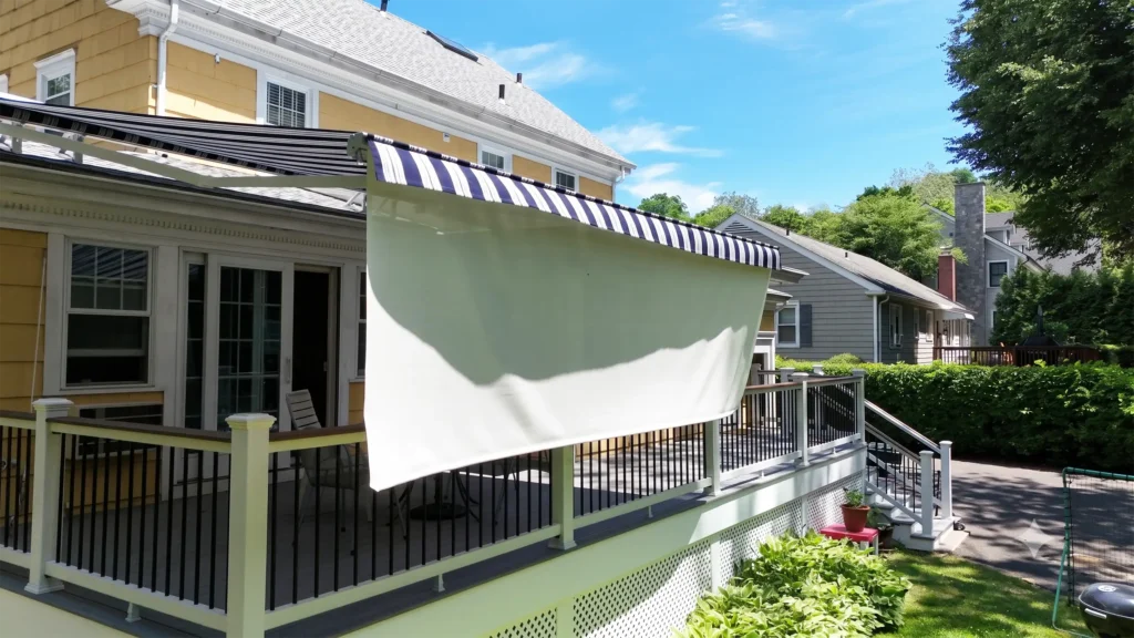 Yellow house with a blue-and-white striped awning over a shaded deck area under a bright blue sky