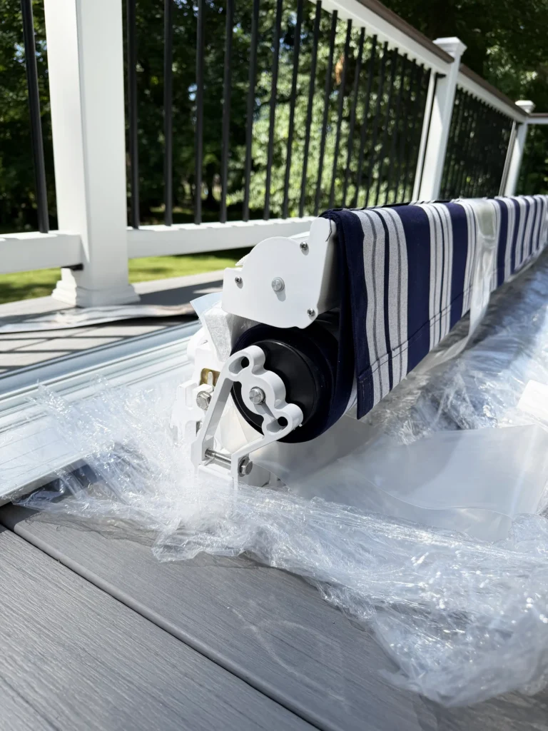 Close-up of a pool cover reel with navy striped fabric on a deck beside a white railing, with water splashing nearby.